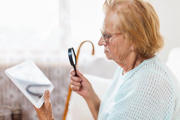 Elderly woman with glasses and loupe using a digital tablet